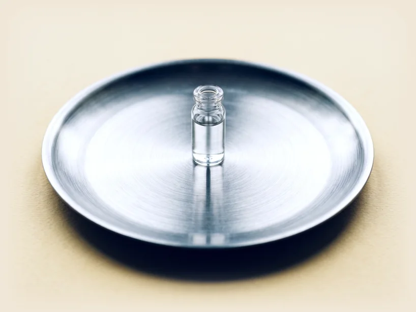 A single plain clear vial standing on a brushed steel plate