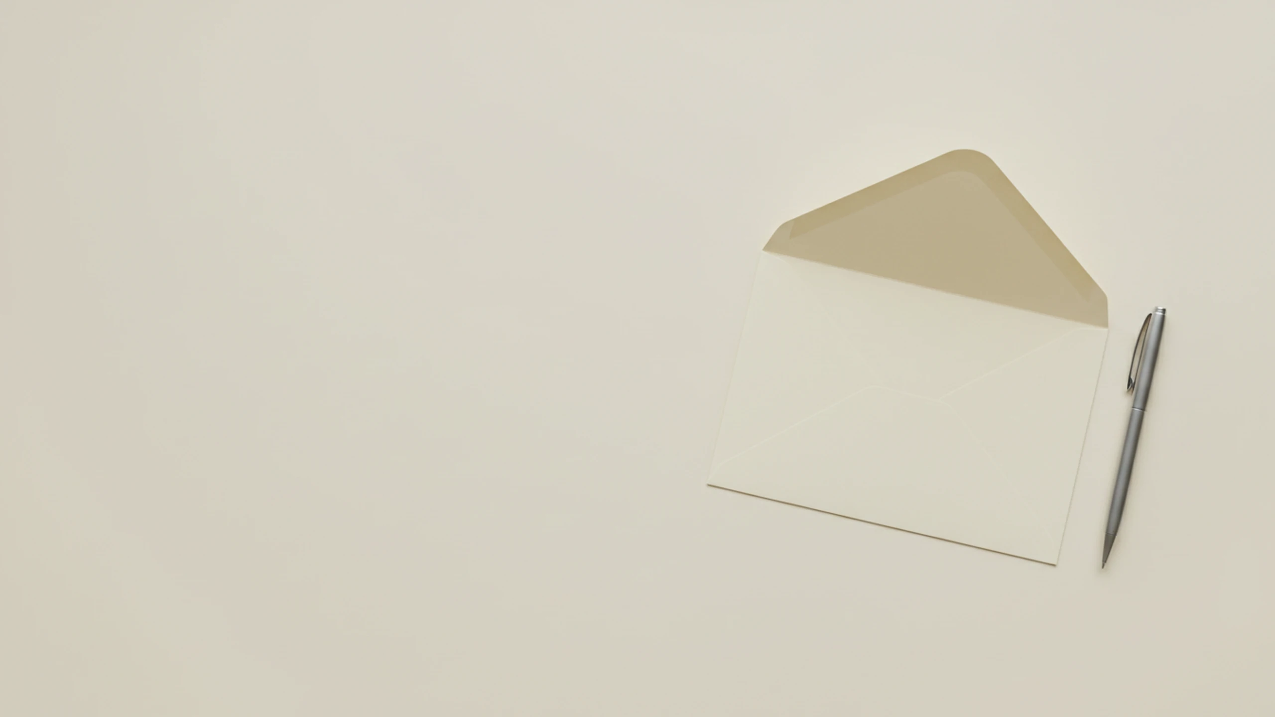 A plain unaddressed cream envelope and a slim steel pen on a flat cream surface